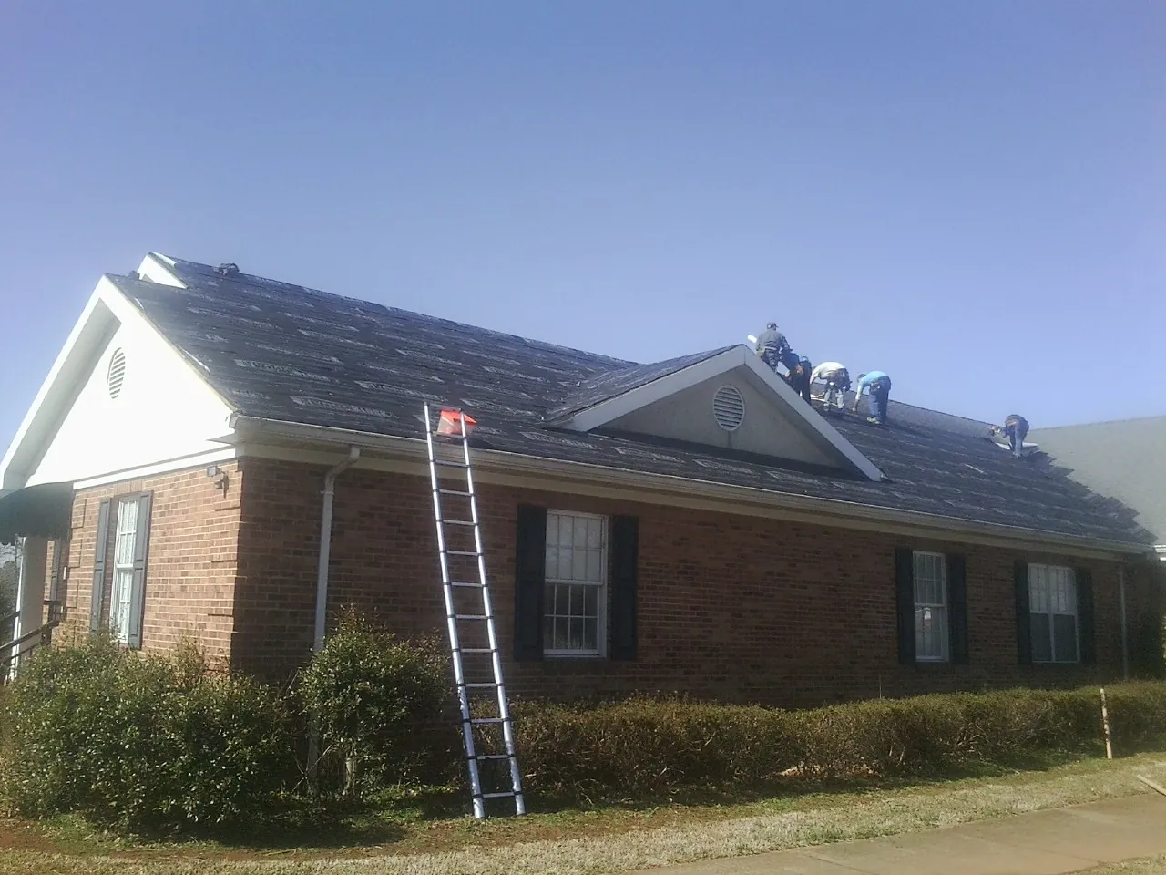 Crew tearing shingles off a brick ranch roof with a ladder set — Metal Roof Repair work by our crew in Woodville