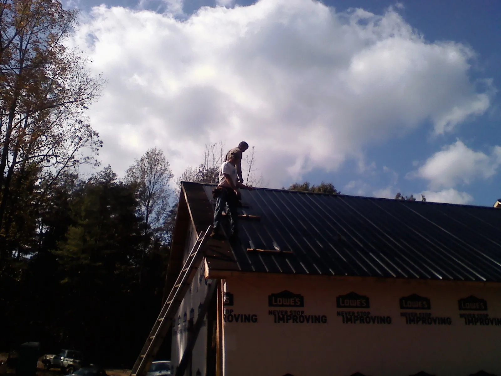 Roofer fastening dark metal panels high against a cloudy sky, from a Roof Inspection job in Woodville